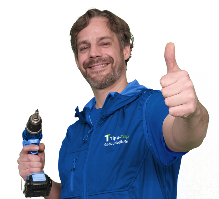 Ein Mitarbeiter für Hausmeisterservice in blauer Arbeitskleidung mit Bohrmachine und Daumen hoch